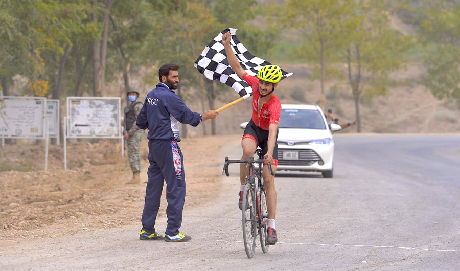 A cyclist touches a flag after crossing the finish line at the first All Pakistan Cycle Race in Orakzai tribal district on September 30, 2021. (Photo Courtesy: KP Tourism and Culture Authority)