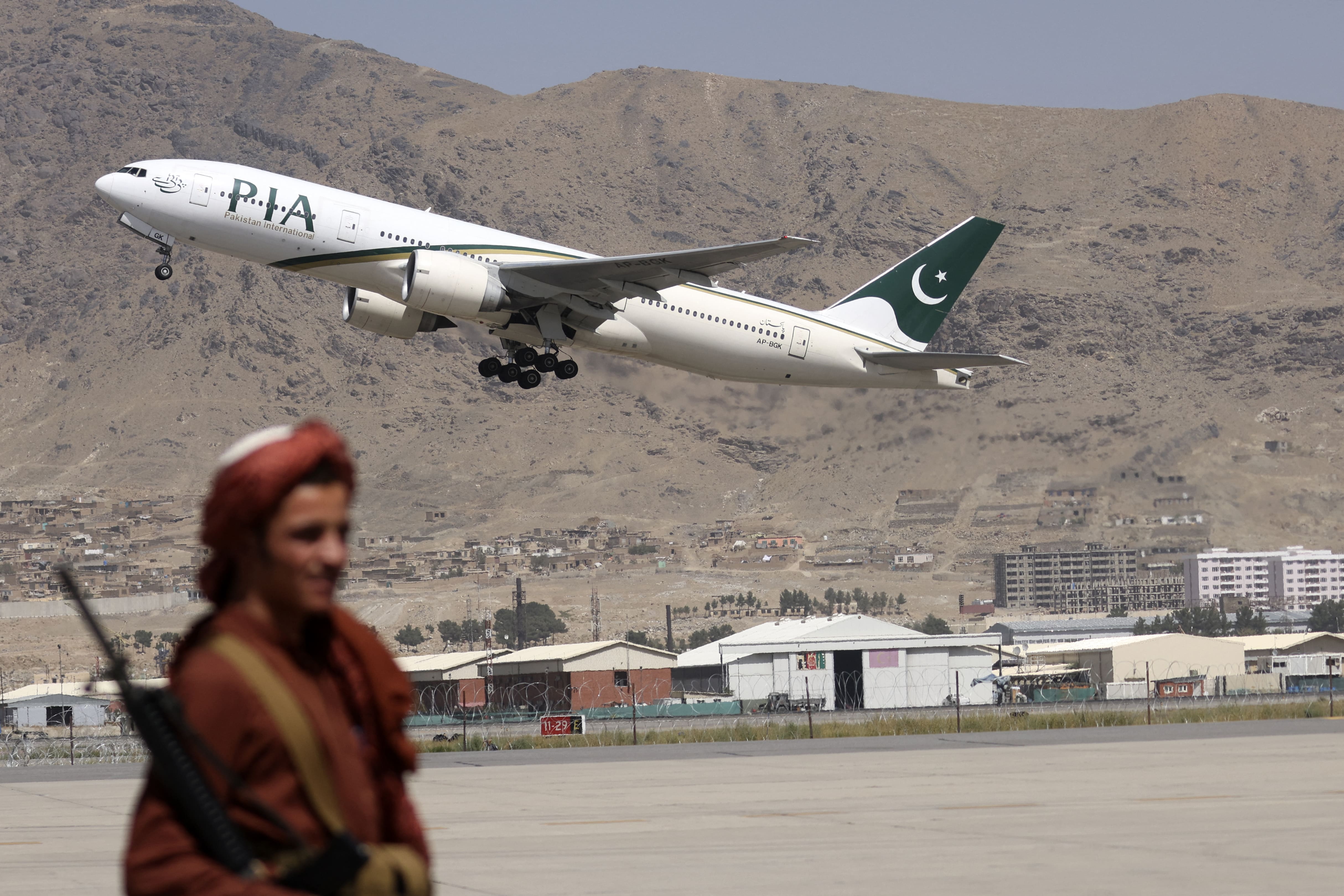 A Taliban fighter stands guard as a Pakistan International Airlines plane, the first commercial international flight to land since the Taliban retook power last month, takes off with passengers onboard at the airport in Kabul on September 13, 2021. (AFP)