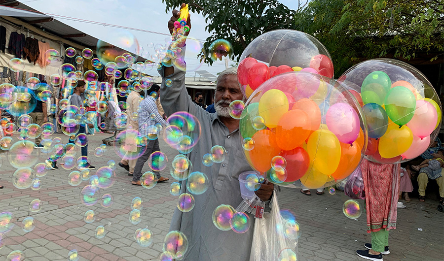 A Pakistani balloon vendor makes bubbles to attract customers at a market in Islamabad, Pakistan, Sunday, Oct. 17, 2021. (AP)