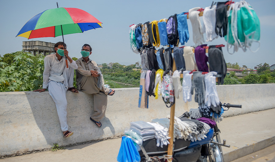Street vendors selling facemasks sit under an umbrella as they wait for customers on a roadside, in Rawalpindi on May 9, 2020. (AFP/ FILE)