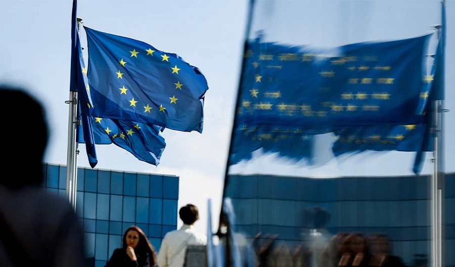 People walk in front of the European Union flag in the area of the EU headquarters in Brussels on September 23, 2021. (AFP)