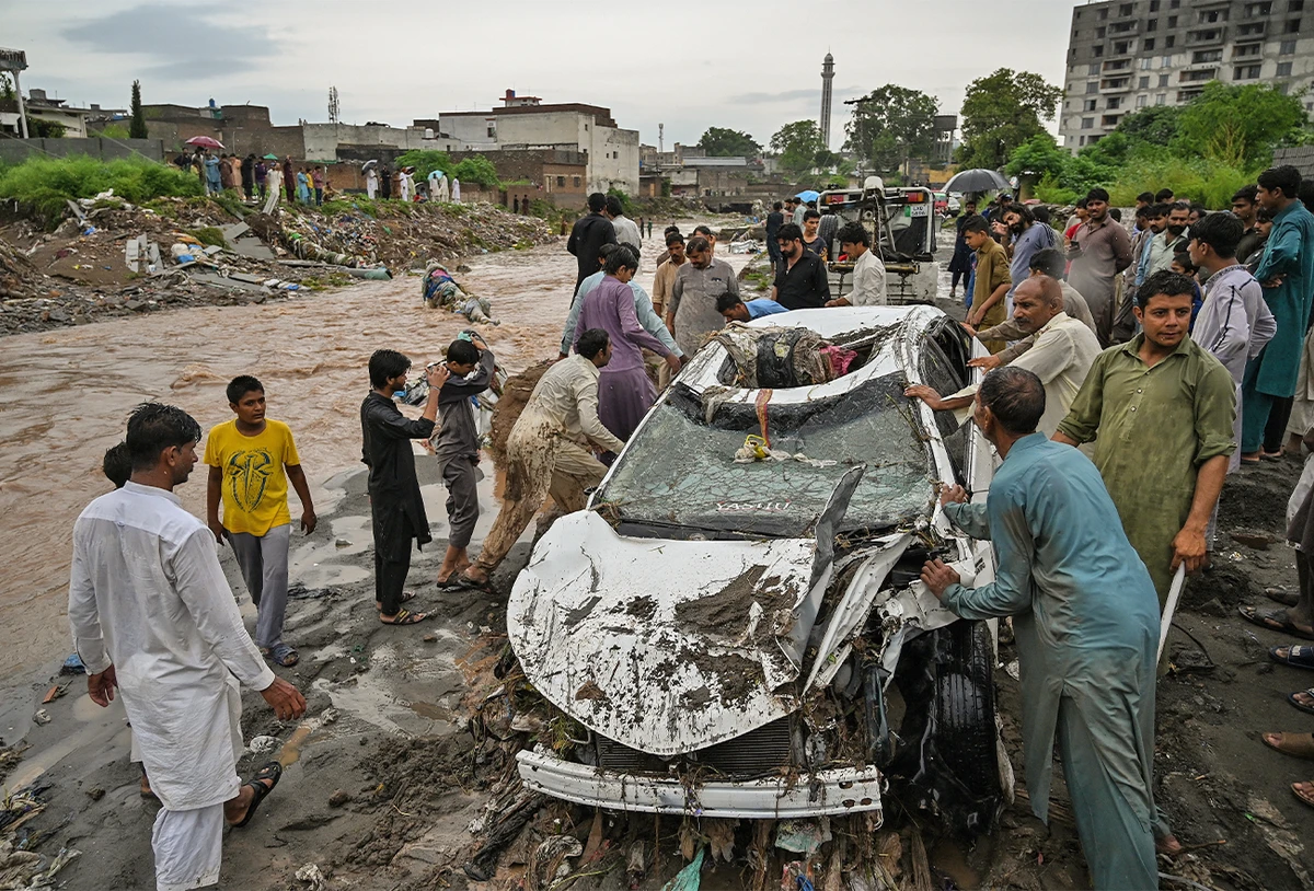 Residents try to move a damaged car stuck in the mud along a street flooded after heavy monsoon rains in Islamabad, Pakistan, on July 28, 2021. (AFP/File)