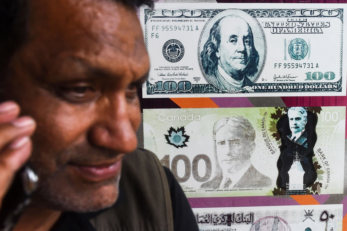 A Pakistani man talks on the phone in front of a poster displaying US dollars at the currency exchange place in Lahore on May 16, 2019. (AFP/ File)