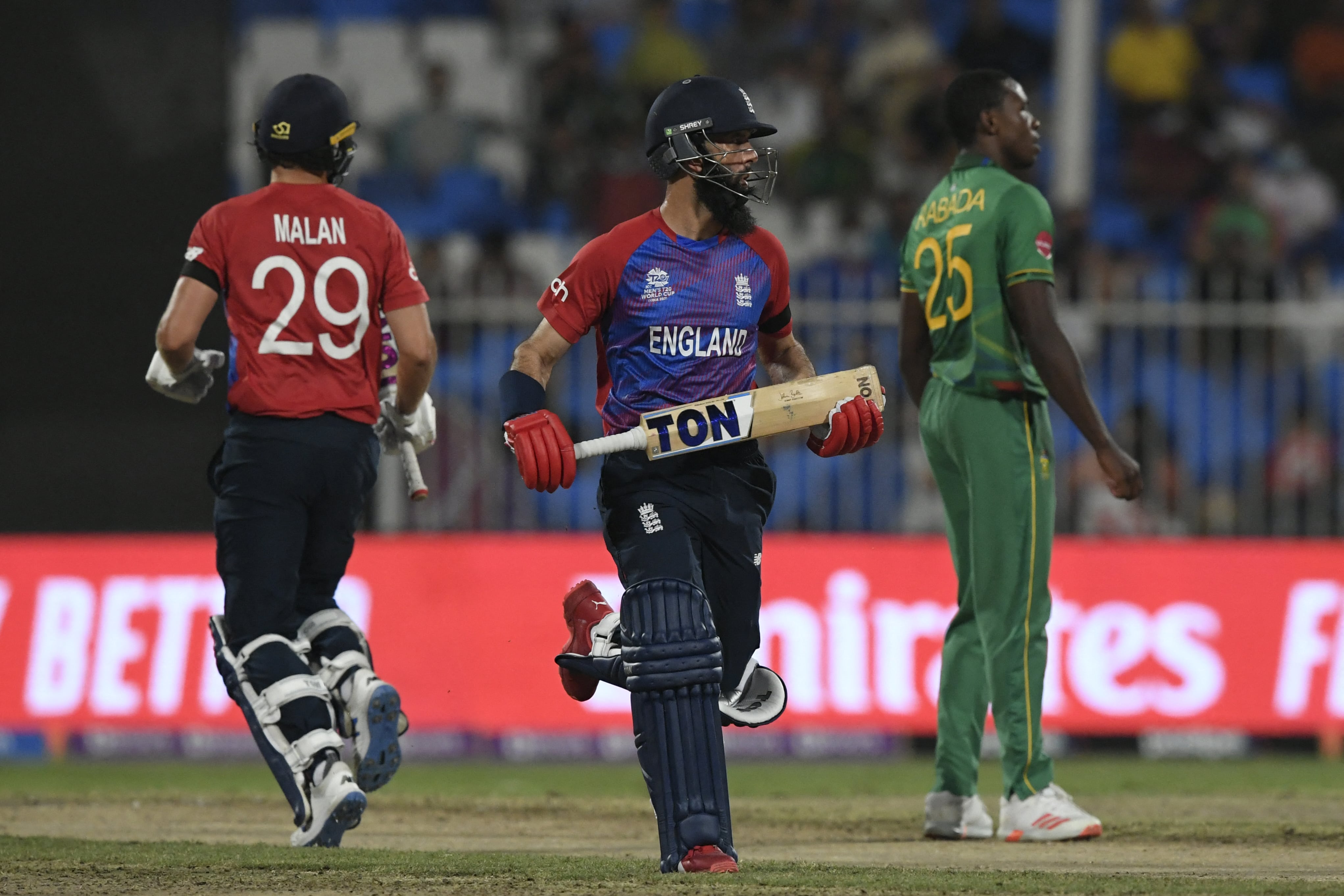 England's Moeen Ali (C) and Dawid Malan (L) run between the wickets as South Africa's Kagiso Rabada watches during the ICC men’s Twenty20 World Cup cricket match between England and South Africa at the Sharjah Cricket Stadium in Sharjah on November 6, 2021. (AFP)
