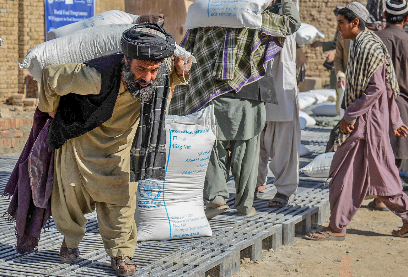Afghan people carry sacks of food grains distributed as an aid by the World Food Programme in Kandahar, Afghanistan, on October 19, 2021. (AFP)