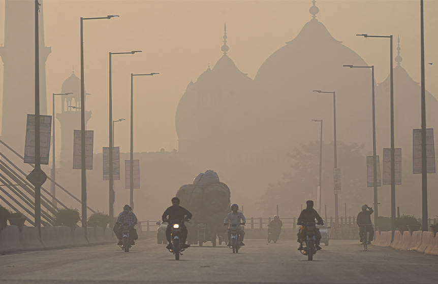 Commuters ride along a road amid smoggy conditions in Lahore on November 16, 2021. (AFP)