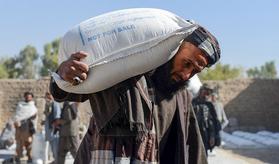 Afghan people carry sacks of food grains distributed as an aid by the World Food Programme (WFP) in Kandahar on October 19, 2021. (AFP)