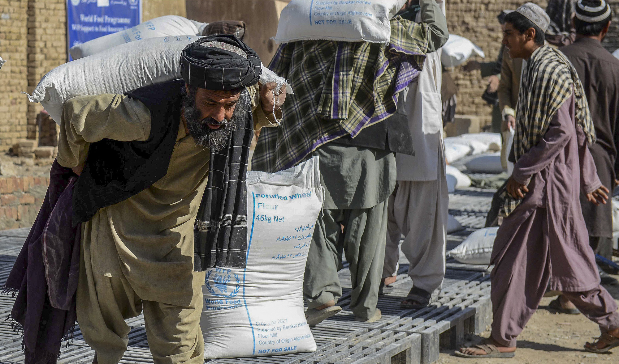 Afghan people carry sacks of food grains distributed as an aid by the World Food Programme (WFP) in Kandahar, Afghanistan, on October 19, 2021. (AFP)