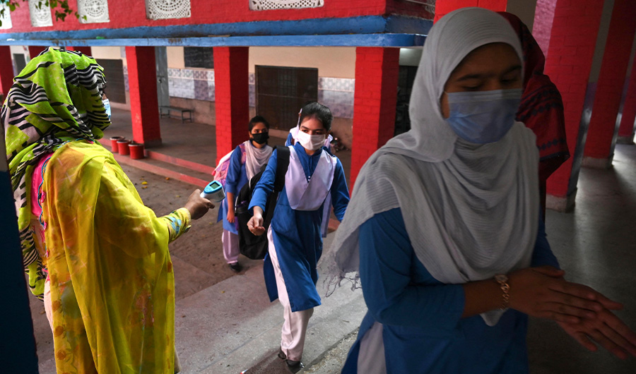 A teacher sprays sanitizer (R) while a colleague (unseen) checks the body temperature of a student in a queue while they arriving at a school in Lahore on September 16, 2021. (AFP)