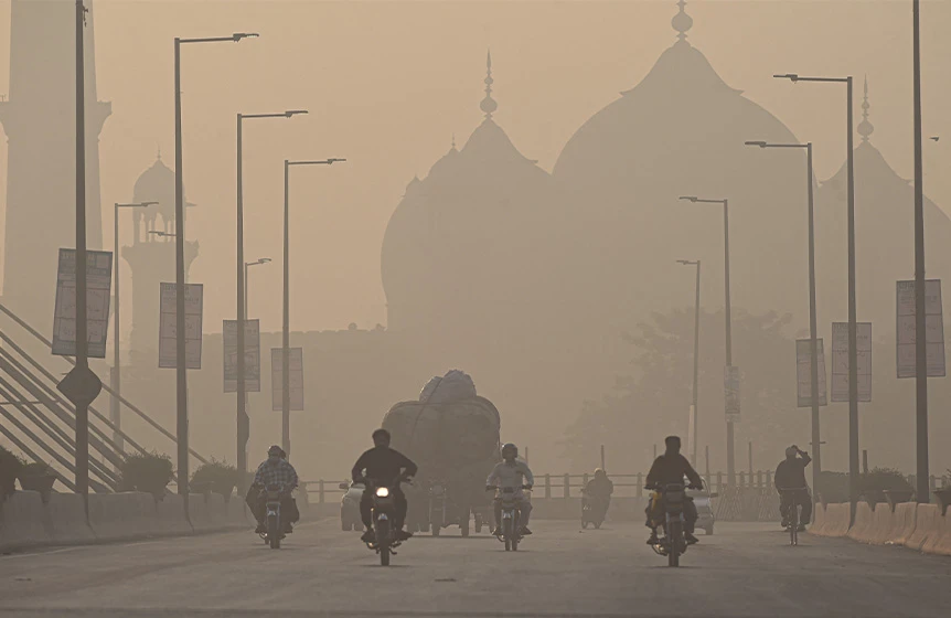 Commuters ride along a road amid smoggy conditions in Lahore on November 16, 2021. (AFP)