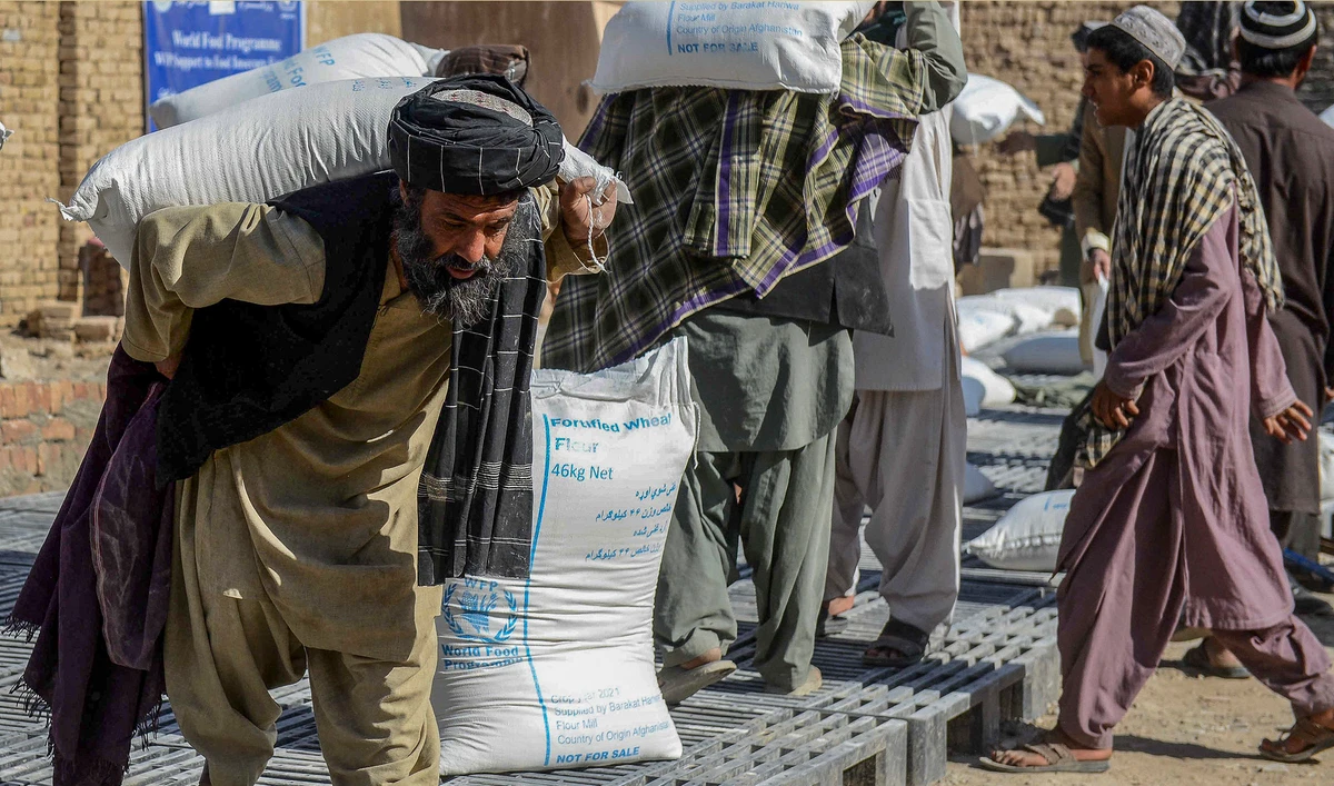Afghan people carry sacks of food grains distributed as an aid by the World Food Programme (WFP) in Kandahar, Afghanistan, on October 19, 2021. (AFP)