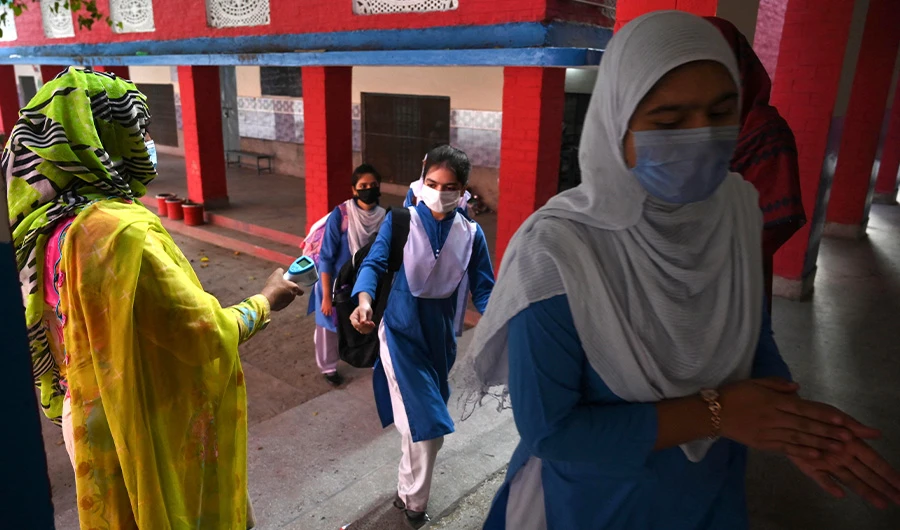 A teacher sprays sanitizer (R) while a colleague (unseen) checks the body temperature of a student in a queue while they arriving at a school in Lahore on September 16, 2021. (AFP)