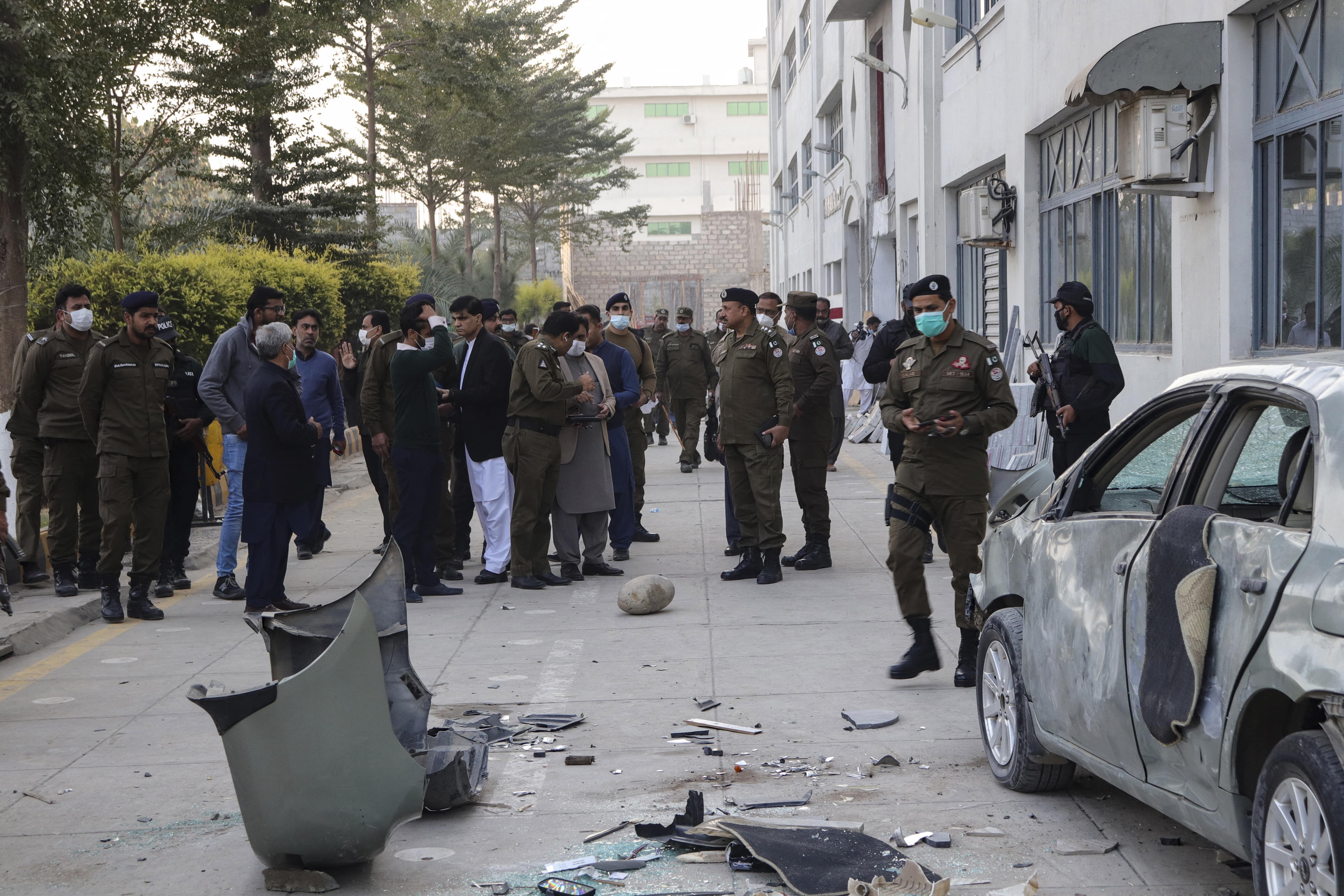 Security officials gather beside a damaged vehicle near the premises of a factory in Sialkot, Pakistan, on December 3, 2021. (AFP)