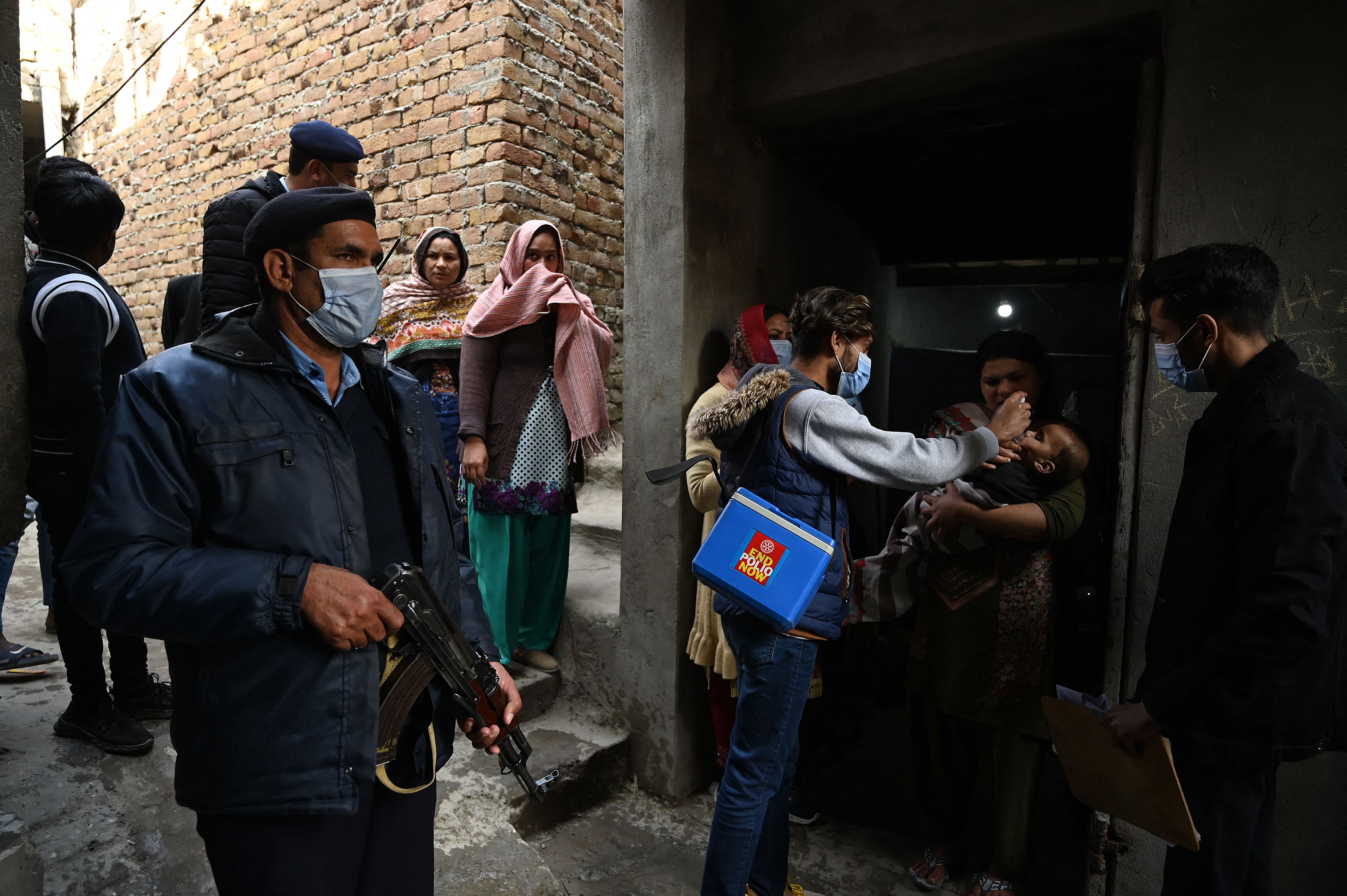 A policeman (L) stands guard as a health worker administers polio vaccine drops to a child during a polio vaccination door-to-door campaign in a slum area in Islamabad on January 13, 2021. (AFP)