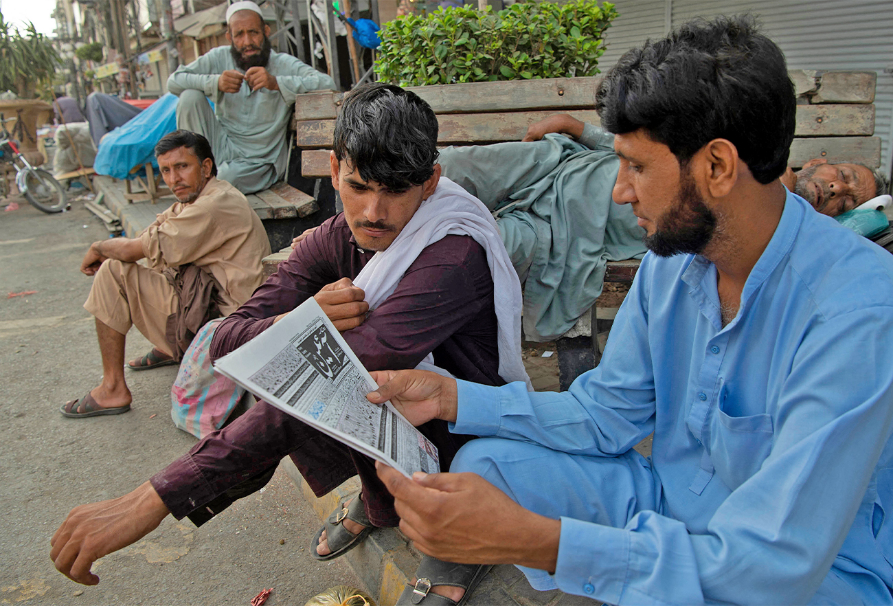 Daily wage labourers sit along the roadside and read a newspaper as they wait to be hired for work a day after the Pakistan government announced the fiscal budget in Peshawar, Pakistan, on June 12, 2021. (AFP/File)