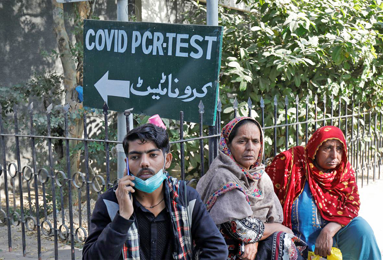 People sit next to a coronavirus disease test sign outside the School of Nursing in Jinnah Postgraduate Medical Centre, in Karachi, Pakistan, on December 9, 2021. (REUTERS)