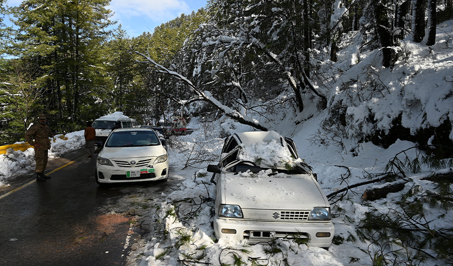 An army soldier stands near a damaged car on a road during a rescue operation to clear roads following a blizzard along the roads to the hill town of Murree, Islamabad on January 9, 2022. (AFP)