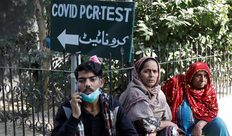 People sit next to a coronavirus disease (COVID-19) test sign outside the School of Nursing in Jinnah Postgraduate Medical Centre (JPMC), in Karachi, Pakistan December 9, 2021. (REUTERS)