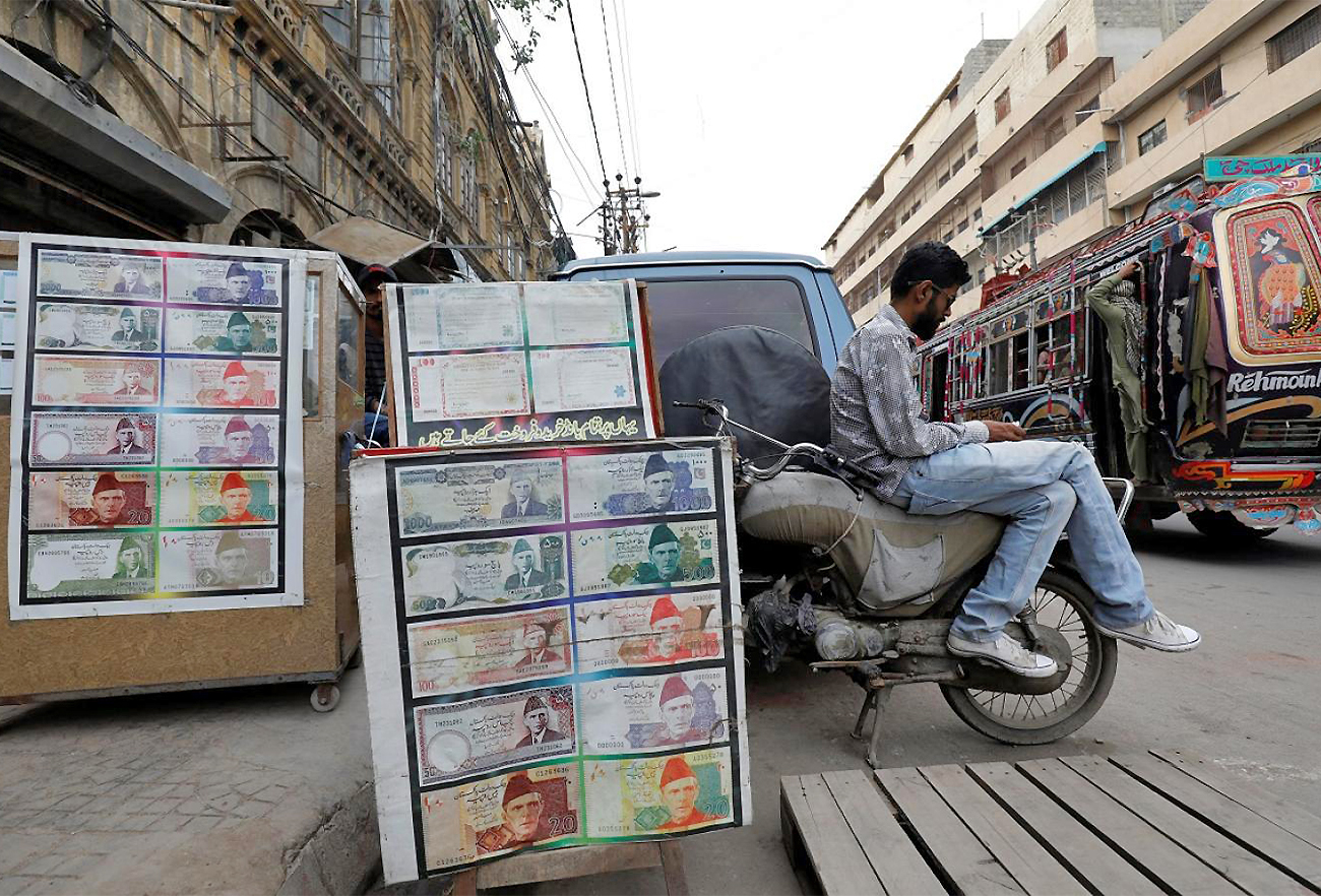 A money changer waits for customers as he sits on a bike beside a money exchange stall decorated with pictures of banknotes in Karachi, Pakistan, on September 30, 2021. (REUTERS/File)