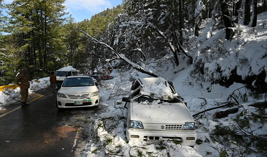 An army soldier stands near a damaged car on a road during a rescue operation to clear roads following a blizzard along the roads to the hill town of Murree, Islamabad on January 9, 2022. (AFP)