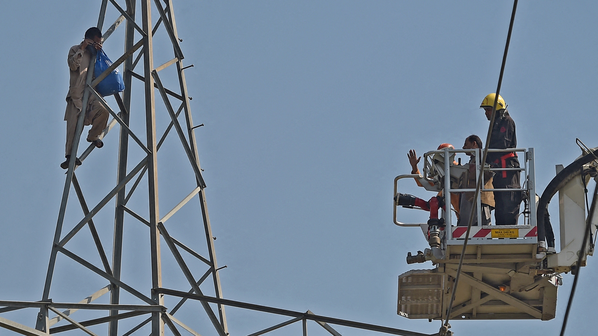 Pakistani rescuers, right, engage with a man who climbed a high tension pylon to commit suicide attempt as a protest for not receiving justice over the murder of his father, in Islamabad on March 9, 2018. (AFP/File)
