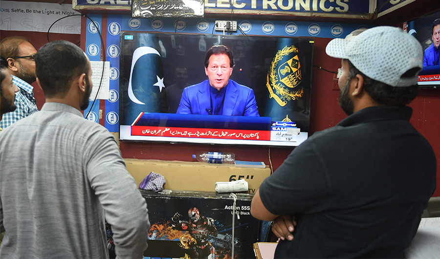 People listen to Pakistan's Prime Minister Imran Khan addressing the nation on television at a market in Karachi on February 28, 2022. (AFP)