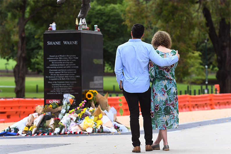 People pay their respects at the base of a statue of former Australian cricket great Shane Warne at the Melbourne Cricket Ground (MCG), in Melbourne on March 5, 2022. (AFP)