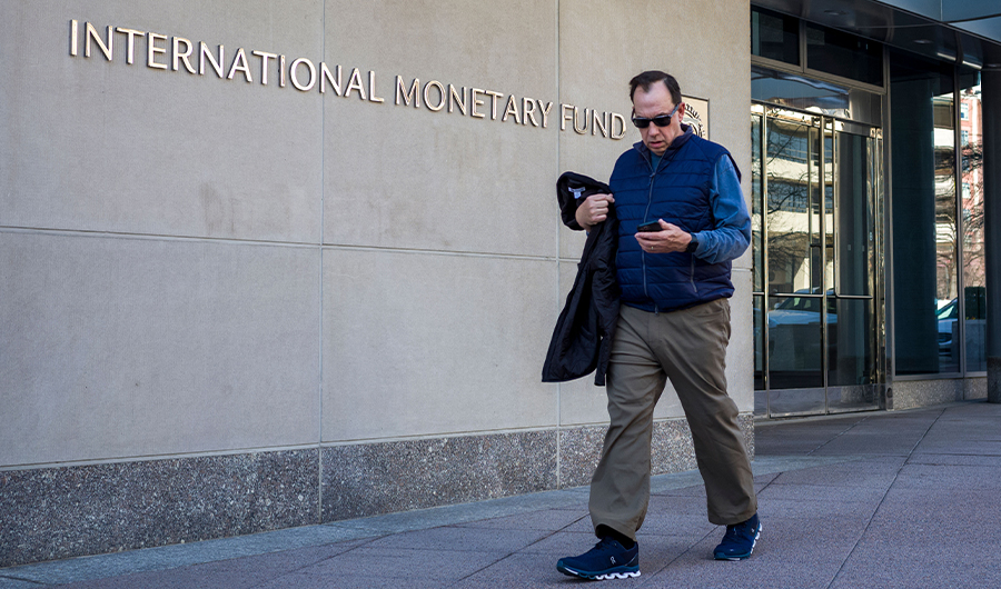 A man looks at his phone as he walks past the International Monetary Fund (IMF) headquarters building in Washington, DC on March 11, 2022. (AFP)