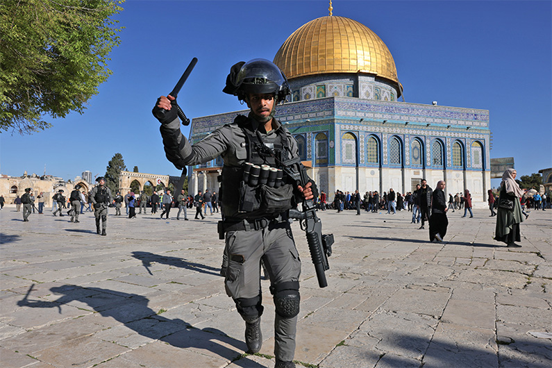 A member of the Israeli security forces lifts his batton in front of the Dome of the Rock mosque at Jerusalem's Al-Aqsa mosque compound, on April 15, 2022. (AFP)