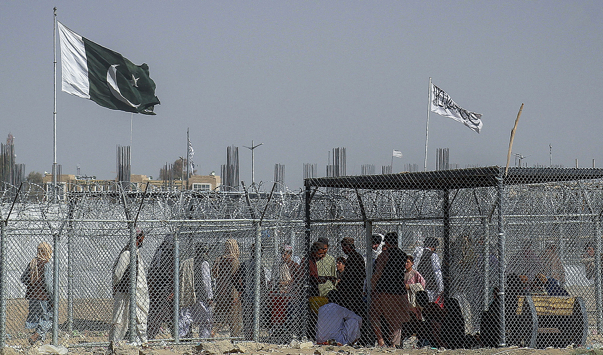 Afghan and Pakistani nationals walk through a security barrier to cross the border as a national flag of Pakistan and a Taliban flag is masted in the Pakistan-Afghanistan border crossing point in Chaman on August 24, 2021. (AFP/File)
