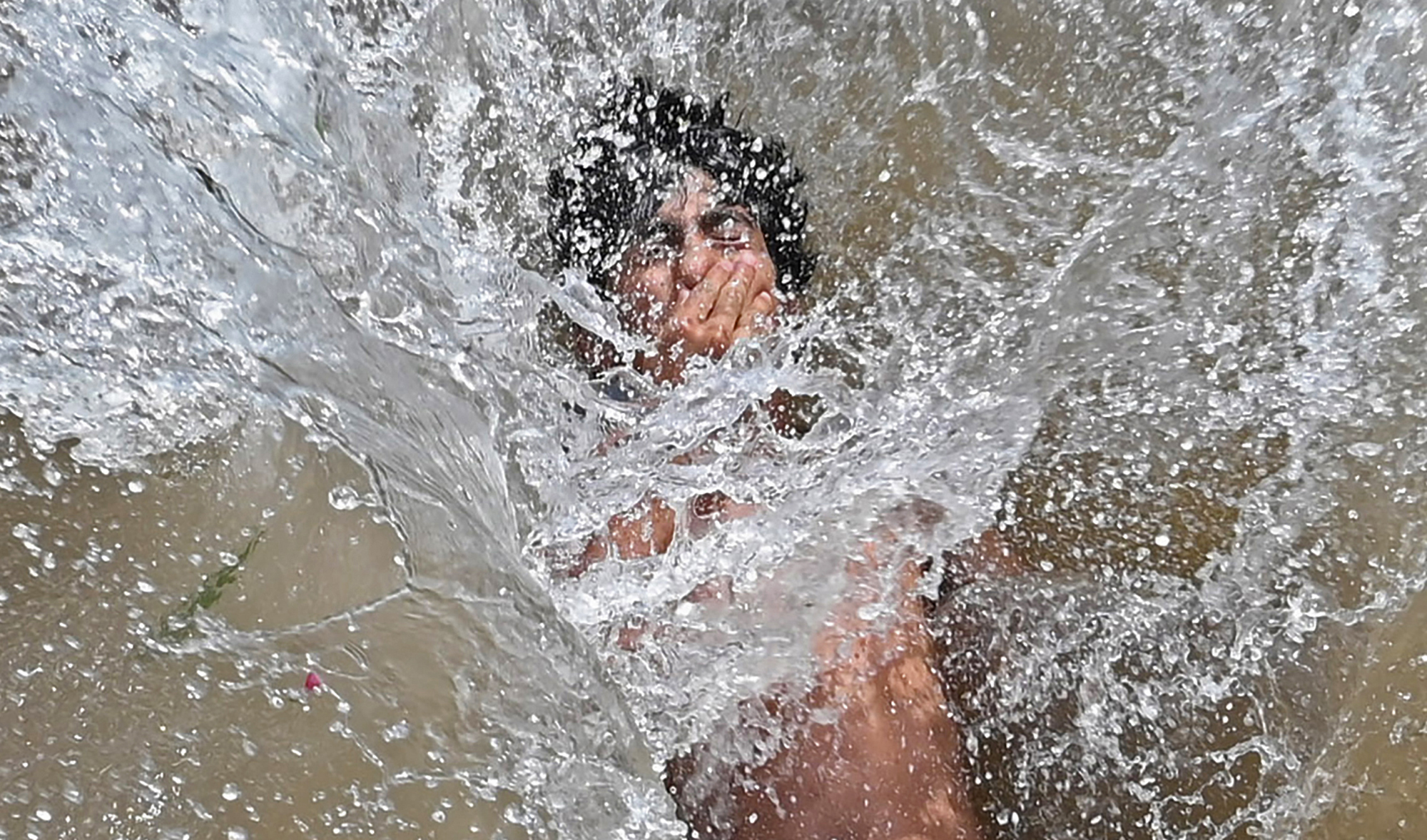 A youth cools himself in a canal during a hot summer day in Lahore, Pakistan, on April 28, 2022. (AFP)
