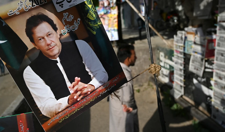 A resident stands beside a picture of Pakistan's Prime Minister Imran Khan as he looks at the morning newspapers displayed for sale at a roadside stall in Islamabad on April 4, 2022. (AFP)