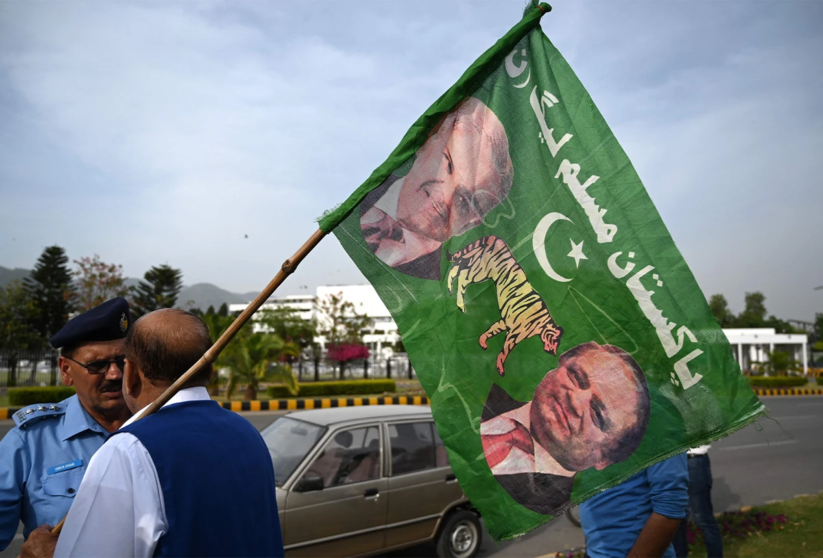 A supporter of Pakistan Muslim League-N (PML-N) holds a party flag with images of Shehbaz Sharif and his elder brother and former prime minister Nawaz Sharif outside the parliament house building in Islamabad, Pakistan, on April 11, 2022. (AFP)