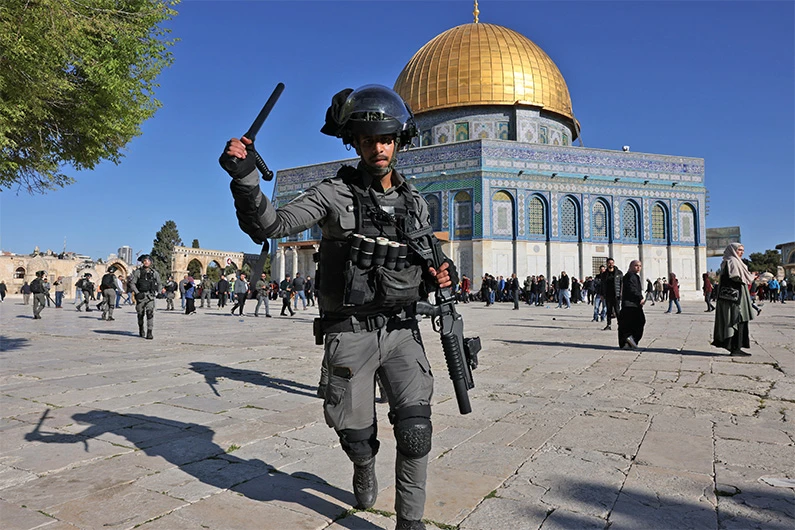 A member of the Israeli security forces lifts his batton in front of the Dome of the Rock mosque at Jerusalem's Al-Aqsa mosque compound, on April 15, 2022. (AFP)