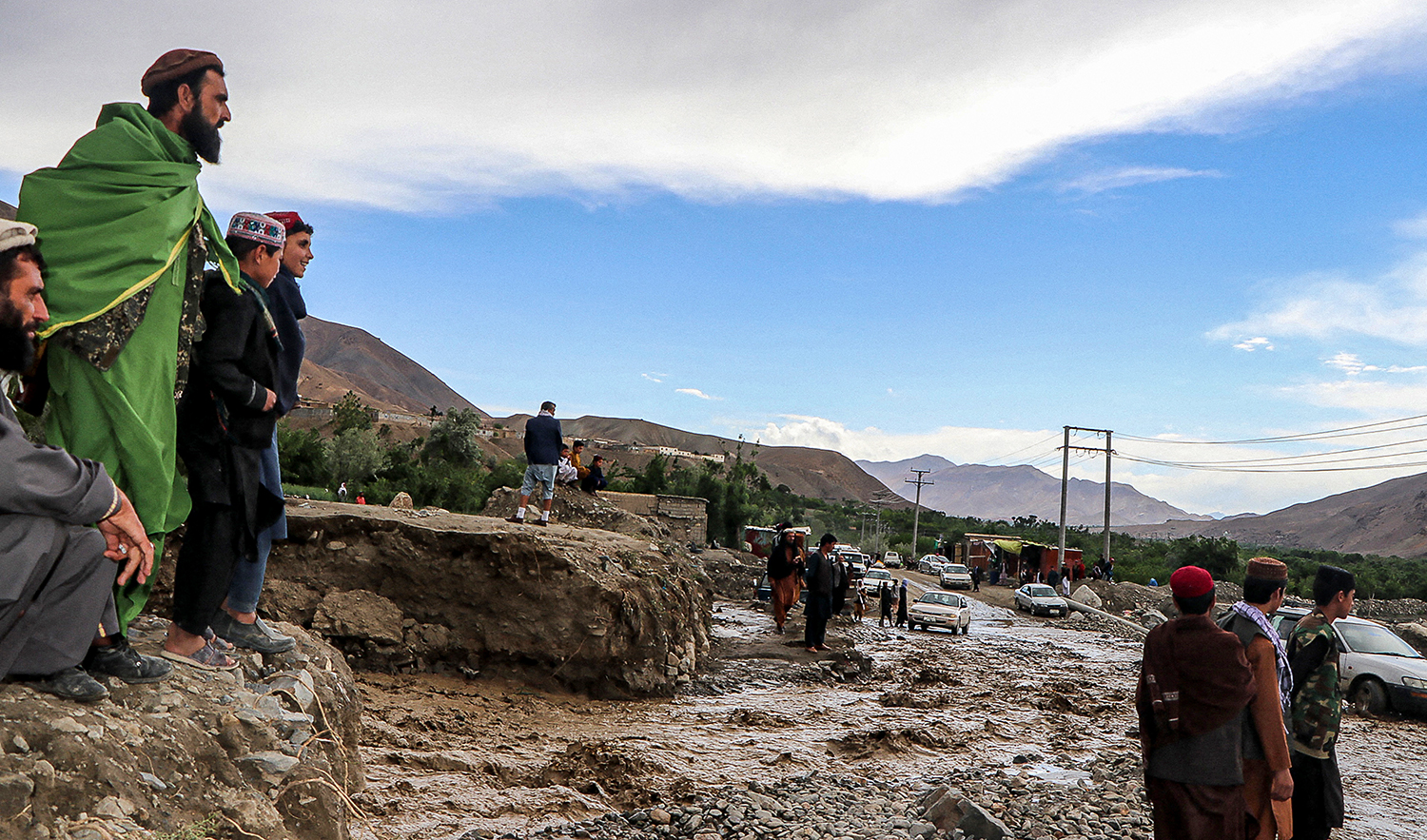 Local residents stand near a road covered in debris and mud a day after flash floods affected in Shinwari District, Parwan Province, Afghanistan on May 5, 2022. (AFP/File)