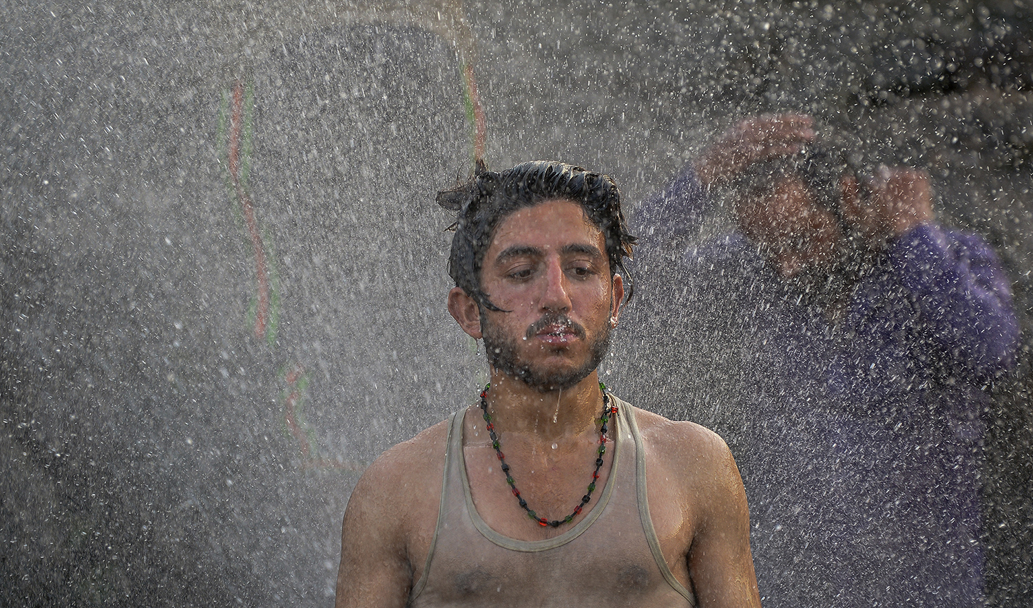 Youth cool off and bathe using a jet of water leaking from a supply pipeline on a hot summer afternoon in Islamabad on April 30, 2022. (AFP/File)