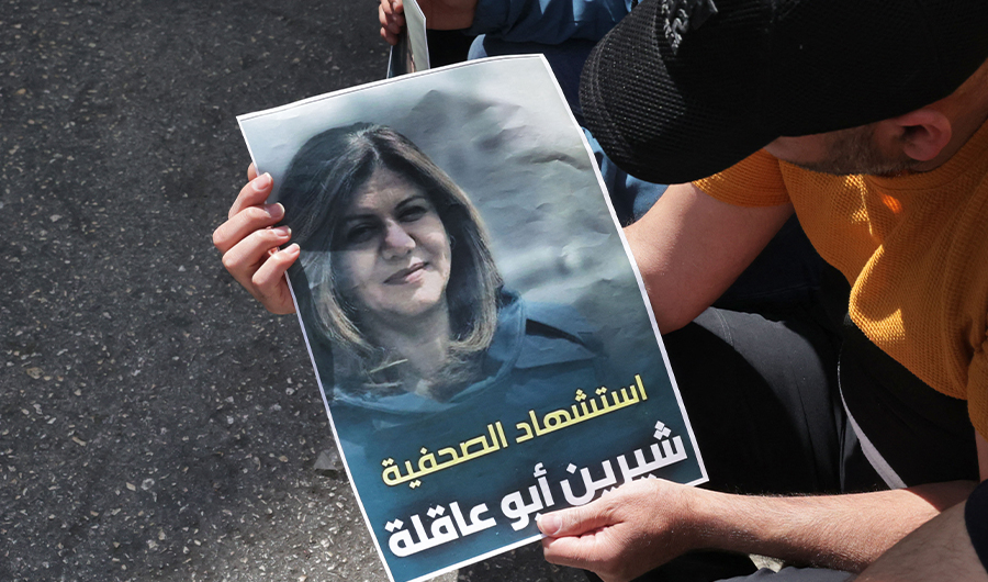Palestinians hold a poster displaying veteran Al Jazeera journalist Shireen Abu Aqleh, who was shot dead as she covered a raid on the West Bank's Jenin refugee camp on May 11, 2022, in the West Bank city of Hebron. (AFP)