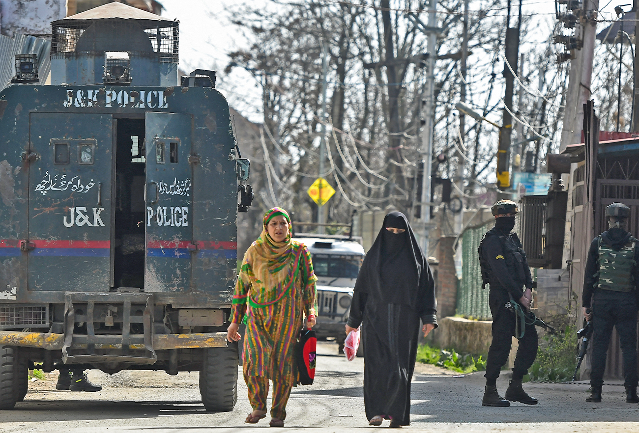 Kashmiri women walks past Indian government forces gathered at Zoonimar area in Srinagar on March 22, 2022. (AFP/File)
