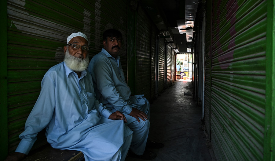 Tailor Muhammad Razzaq (2L) sits outside his shop in Islamabad on April 29, 2022. (AFP)