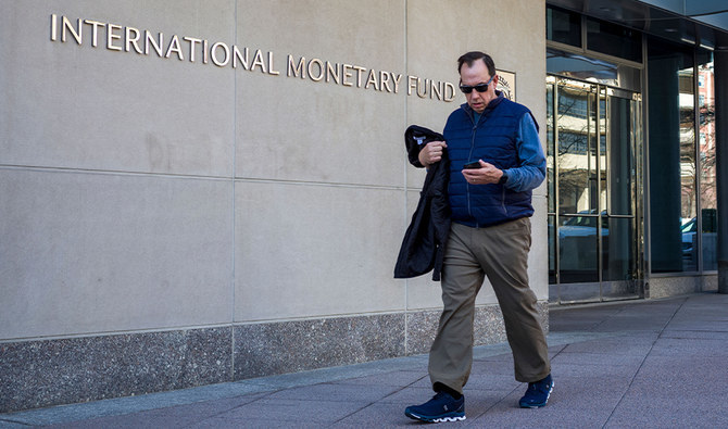 A man looks at his phone as he walks past the International Monetary Fund (IMF) headquarters building in Washington, DC on March 11, 2022. (AFP/FILE)
