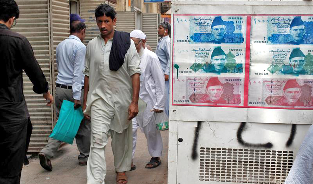 Passersby walk past an advertisement board with photos of the Pakistani rupee at a money exchange along a sidewalk in Karachi, Pakistan, on June 11, 2018. (REUTERS/File)