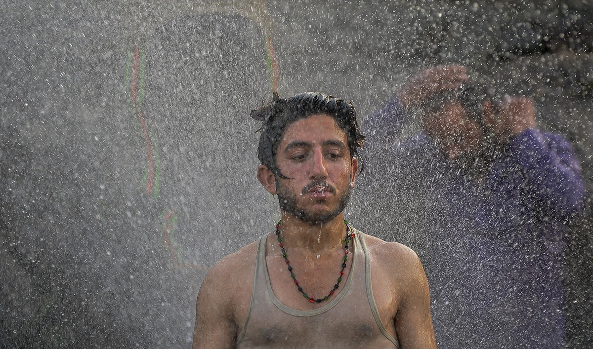Youth cool off and bathe using a jet of water leaking from a supply pipeline on a hot summer afternoon in Islamabad on April 30, 2022. (AFP/File)