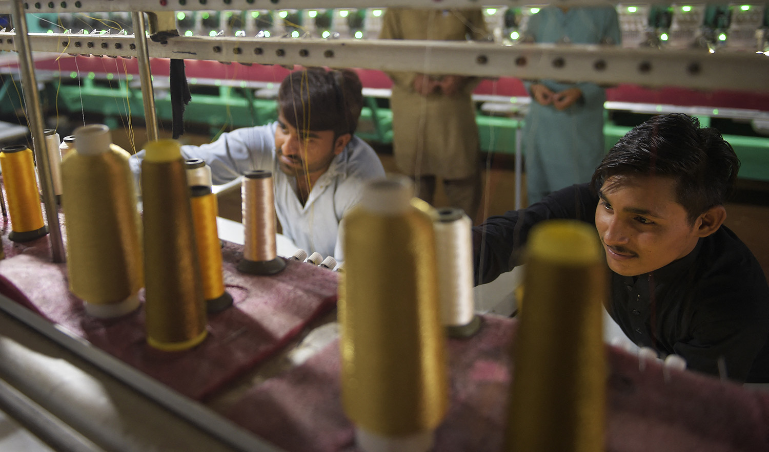 Workers supervise embroidery machines working on fabrics for wedding dresses at a small factory on the outskirts of Islamabad, Pakistan, on September 2, 2020. (AFP/File)