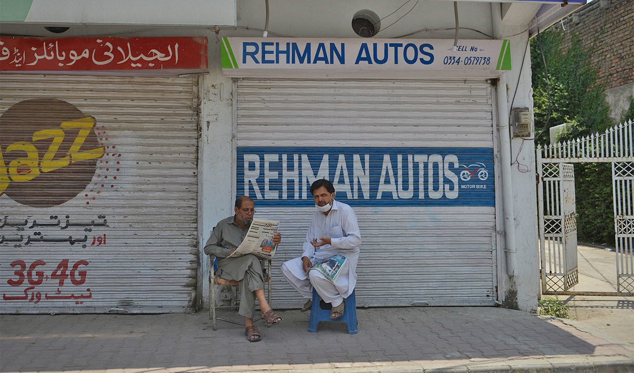 Residents read newspapers near a market which was sealed by the authorities in Rawalpindi, Pakistan, on June 21, 2020. (AFP/File)