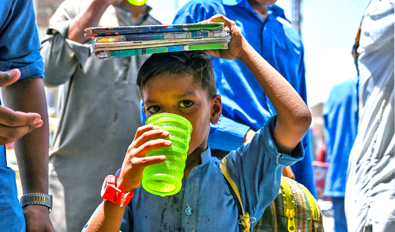 In this picture taken on May 12, 2022, people drink water being distributed by volunteers along a street during a heatwave in Jacobabad. (AFP)