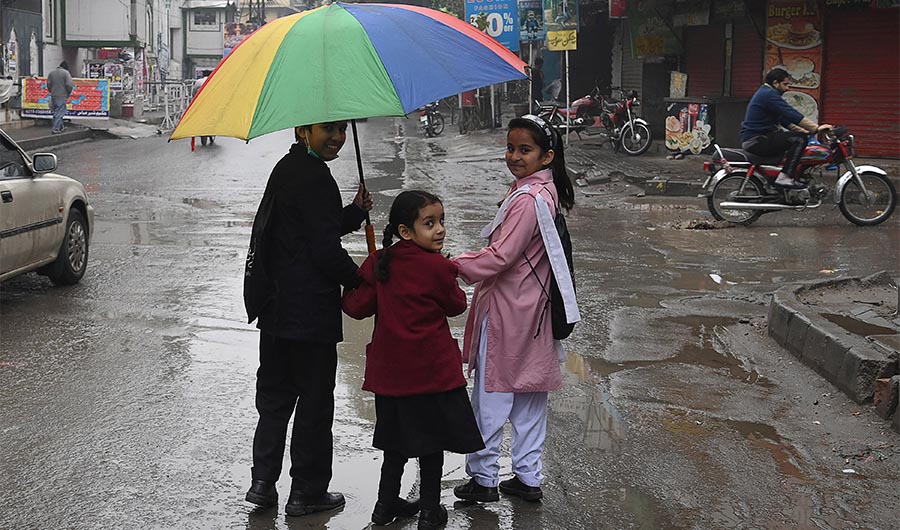 Students walk under an umbrella while returning from school during a rain shower in Lahore on January 22, 2022. (AFP)