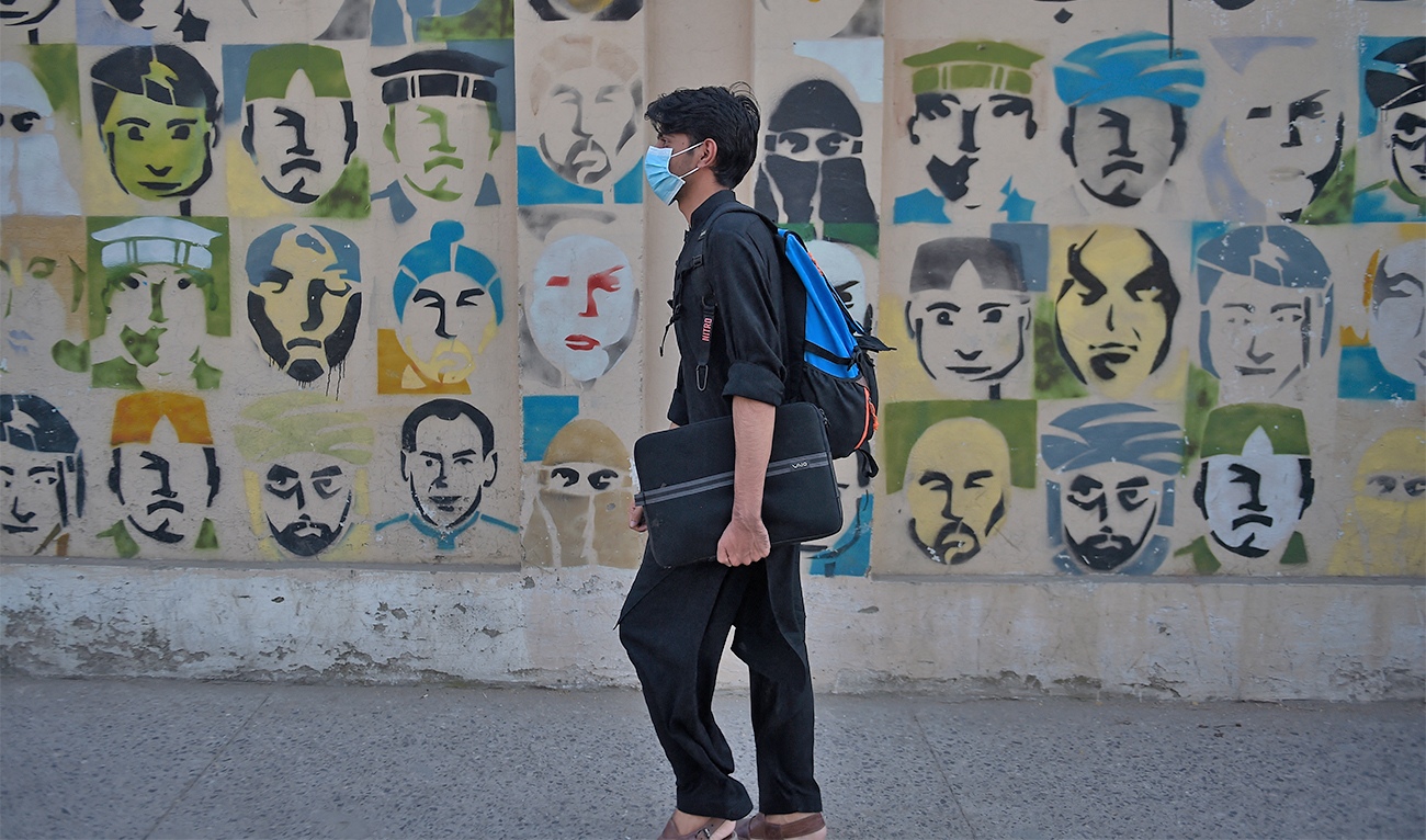 A student wearing a face mask walks past a wall mural on a street in Rawalpindi, Pakistan, on October 6, 2020. (AFP/File)