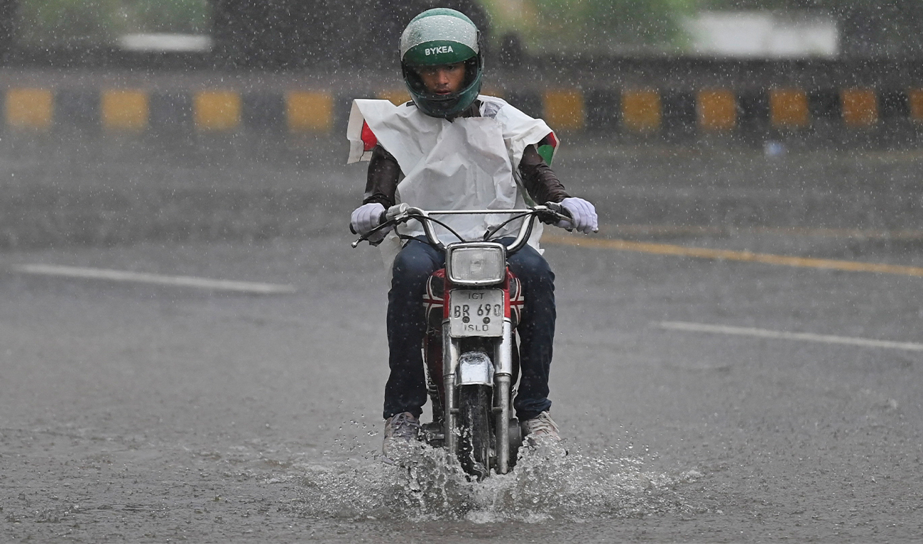 A motorcyclist covered with plastic sheet rides along a street during an early monsoon rainfall in Islamabad, Pakistan on June 21, 2022. (AFP)