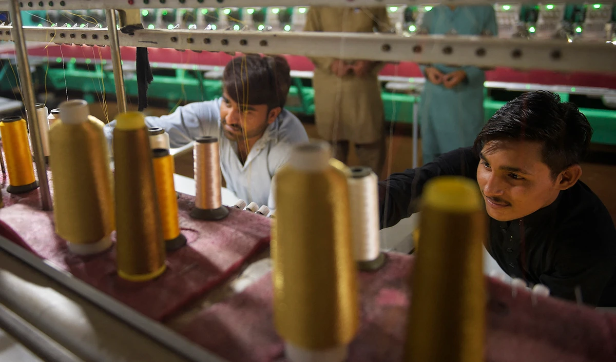 Workers supervise embroidery machines working on fabrics for wedding dresses at a small factory on the outskirts of Islamabad, Pakistan, on September 2, 2020. (AFP/File)
