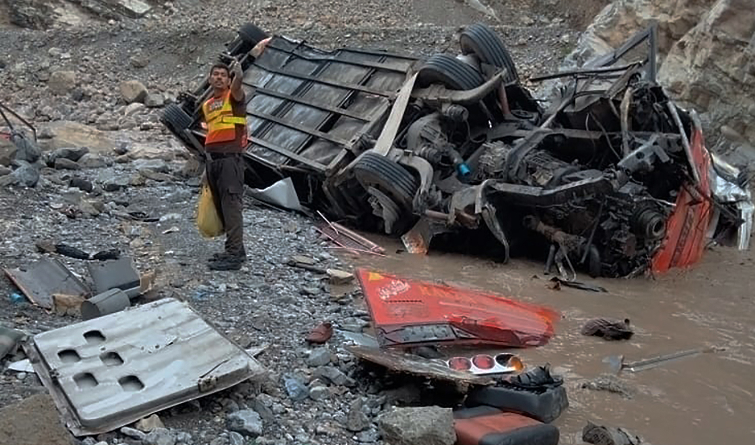In this photo provided by Baluchistan's rescue department, a rescue worker stands next to the wreck of a passenger bus, in Zhob, Baluchistan province, in southwest Pakistan, Sunday, July 3, 2022. (Baluchistan Rescue Department via AP)
